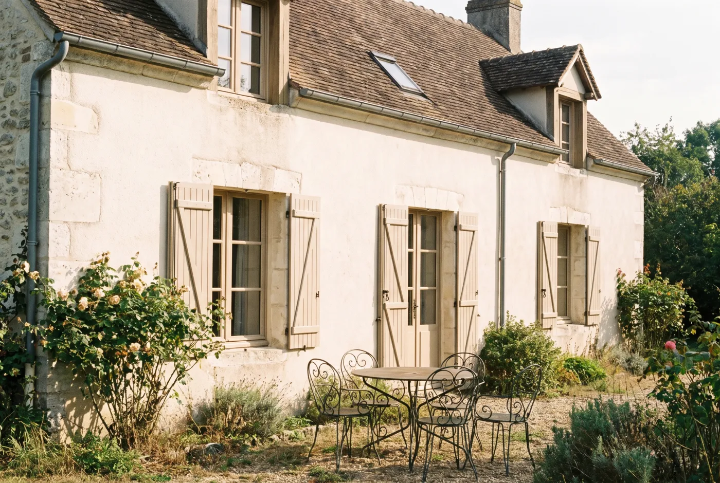 Maison de famille en pierre, volets fermés, vue depuis le jardin